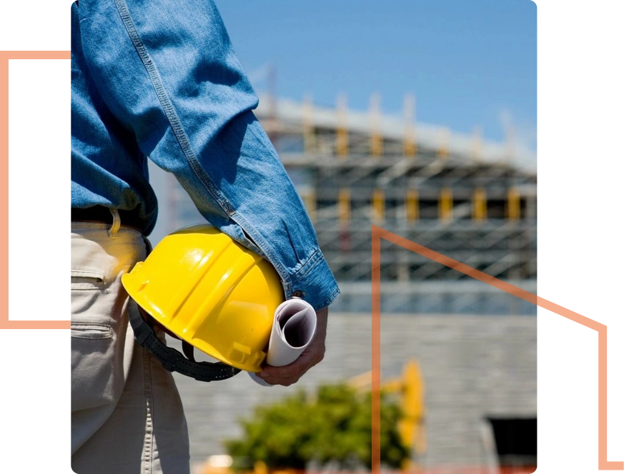 A person holding a yellow hard hat and rolled-up papers stands at a bustling commercial construction site with scaffolding in the background, representing seamless integration of commercial construction services.